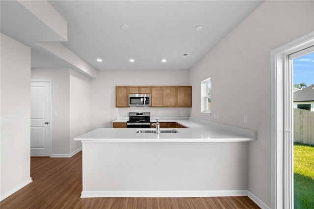 kitchen with sink, appliances with stainless steel finishes, kitchen peninsula, a healthy amount of sunlight, and hardwood / wood-style floors