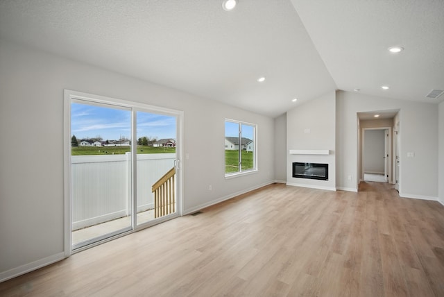 unfurnished living room featuring recessed lighting, lofted ceiling, light wood finished floors, and a glass covered fireplace