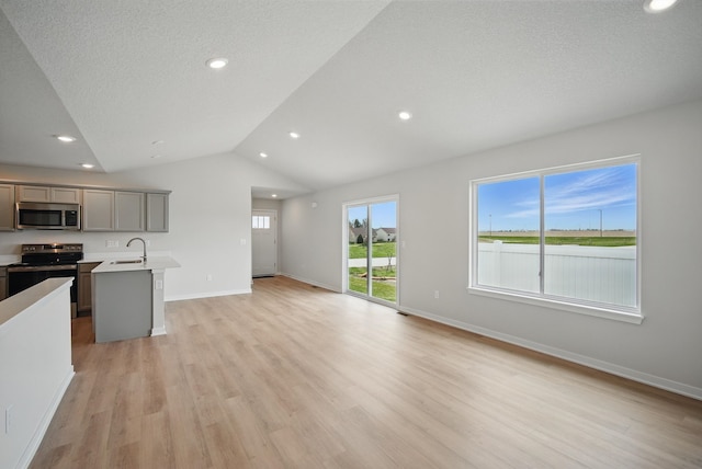 unfurnished living room with recessed lighting, a sink, light wood-style flooring, baseboards, and lofted ceiling