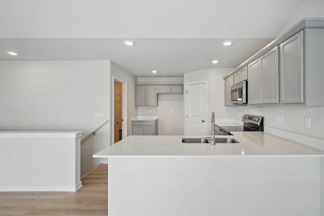 kitchen featuring recessed lighting, appliances with stainless steel finishes, light wood finished floors, a sink, and a peninsula