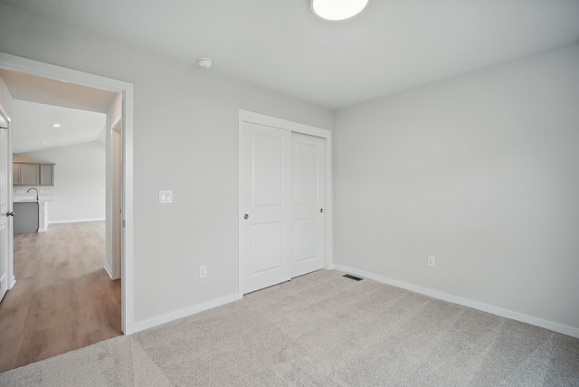 unfurnished bedroom featuring a closet, vaulted ceiling, light carpet, baseboards, and visible vents