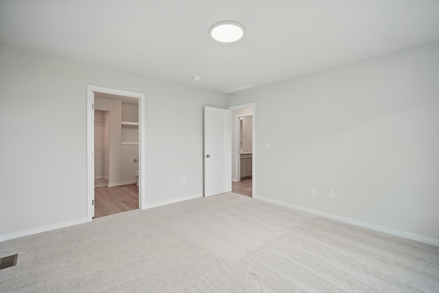 unfurnished bedroom with baseboards, a walk in closet, and light colored carpet