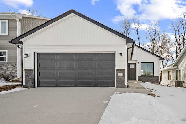 view of front of property featuring an attached garage, central AC, concrete driveway, stone siding, and board and batten siding