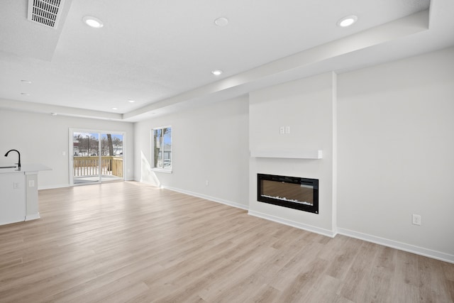 unfurnished living room with light wood-style floors, recessed lighting, visible vents, and a glass covered fireplace