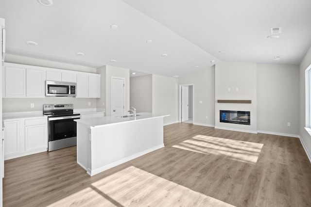 kitchen featuring stainless steel appliances, light countertops, open floor plan, a kitchen island with sink, and white cabinetry