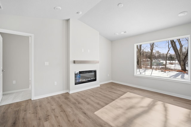 unfurnished living room featuring a glass covered fireplace, baseboards, vaulted ceiling, and light wood finished floors