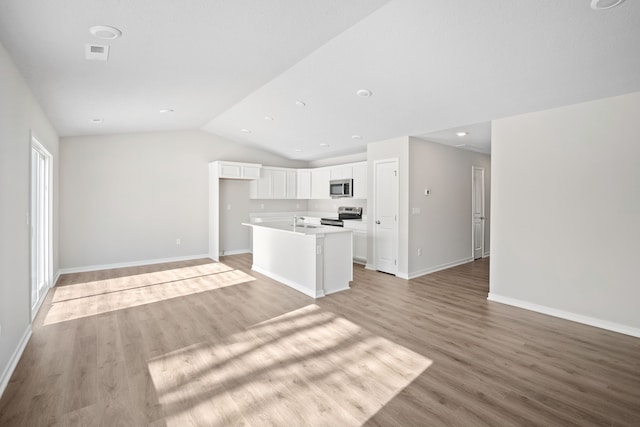 kitchen with white cabinets, a kitchen island, open floor plan, stainless steel appliances, and light countertops