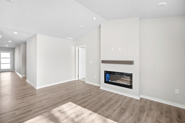 unfurnished living room featuring light wood finished floors, baseboards, vaulted ceiling, and a glass covered fireplace