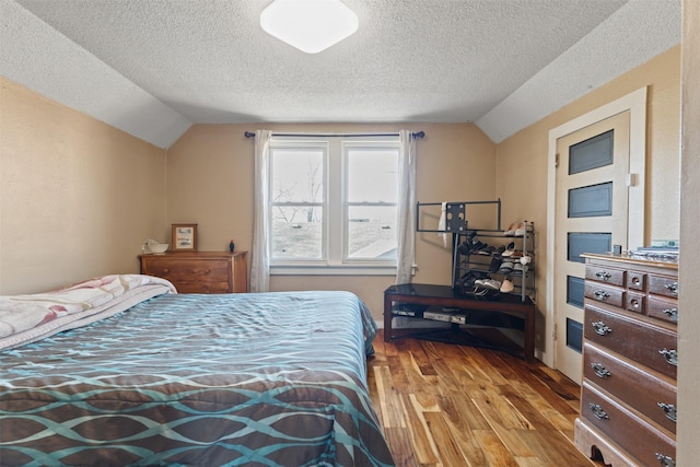 bedroom featuring light hardwood / wood-style flooring, a textured ceiling, and vaulted ceiling