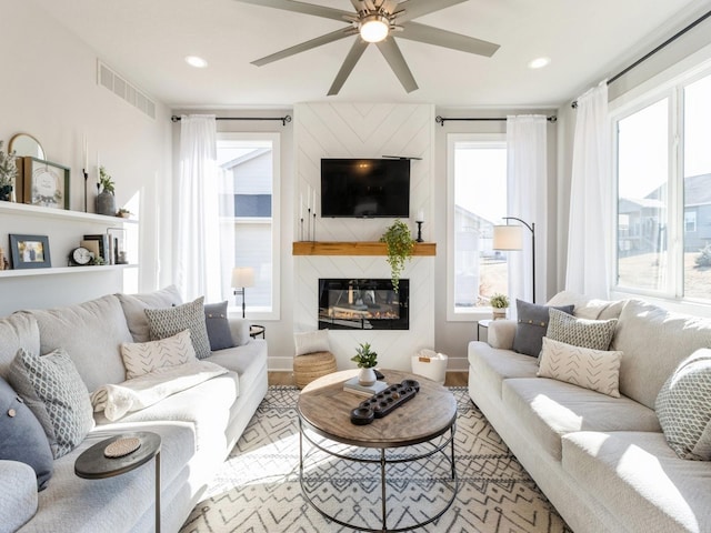 living room featuring ceiling fan, a fireplace, light hardwood / wood-style floors, and a wealth of natural light