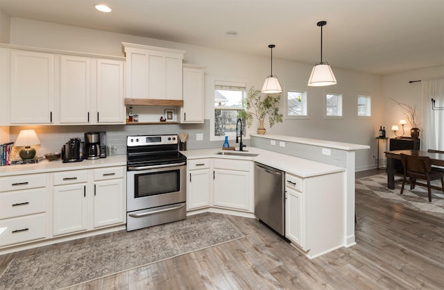 kitchen featuring pendant lighting, sink, appliances with stainless steel finishes, white cabinetry, and kitchen peninsula