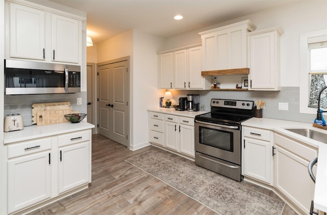 kitchen featuring white cabinetry, backsplash, light hardwood / wood-style floors, and appliances with stainless steel finishes