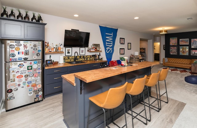 kitchen with a kitchen bar, sink, wooden counters, light wood-type flooring, and stainless steel fridge