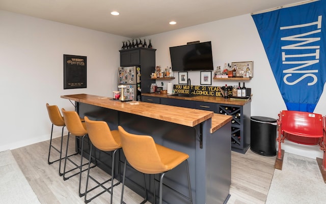 bar with sink, stainless steel fridge, butcher block countertops, and light hardwood / wood-style floors