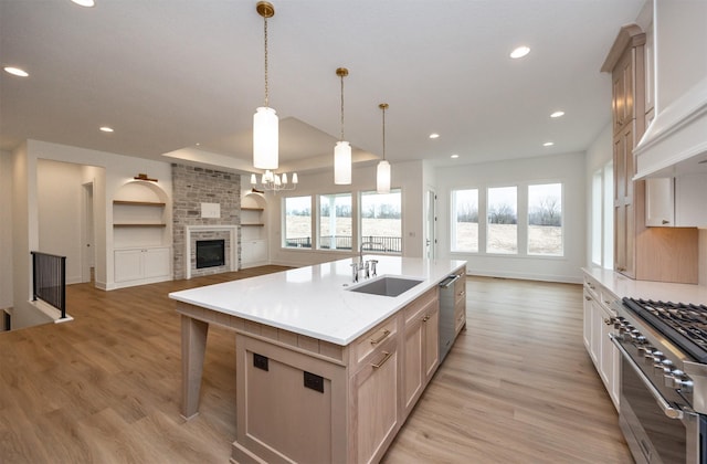 kitchen featuring appliances with stainless steel finishes, decorative light fixtures, sink, light brown cabinets, and a center island with sink