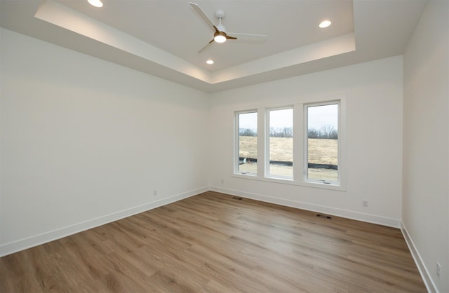 spare room with a tray ceiling, light hardwood / wood-style flooring, and ceiling fan