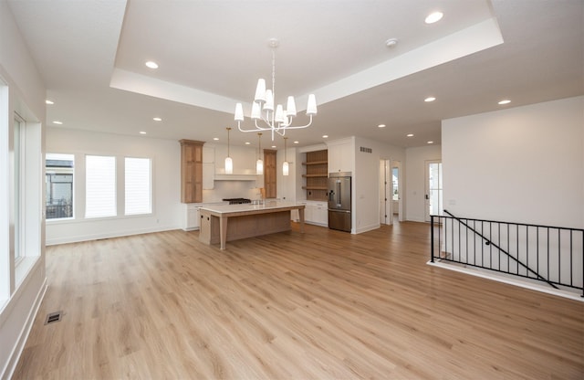 kitchen with a breakfast bar area, high end fridge, a tray ceiling, a kitchen island, and decorative light fixtures