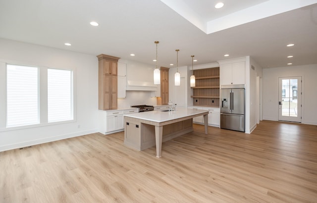 kitchen with decorative light fixtures, white cabinets, a kitchen island with sink, stainless steel appliances, and light hardwood / wood-style flooring