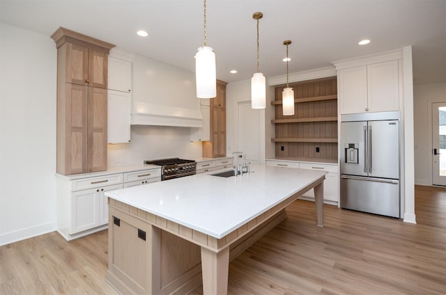 kitchen with high end appliances, sink, pendant lighting, and an island with sink