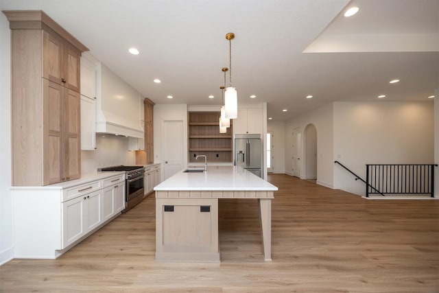 kitchen with pendant lighting, premium range hood, high end appliances, light hardwood / wood-style floors, and a center island with sink