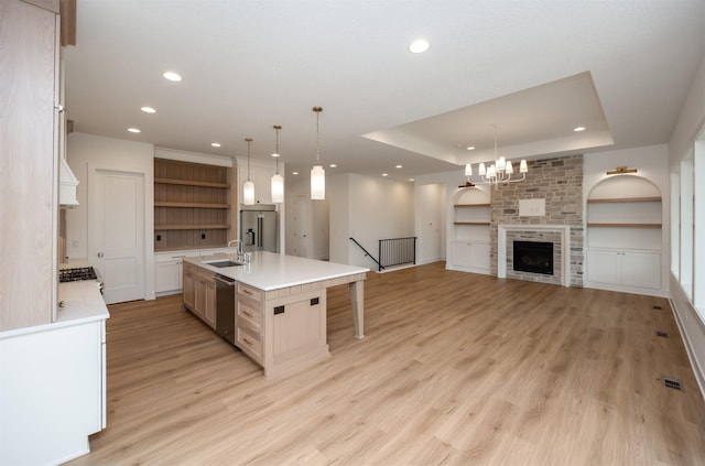 kitchen featuring sink, a large island with sink, stainless steel appliances, a raised ceiling, and light wood-type flooring