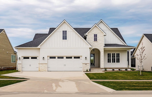 view of front of property with concrete driveway, board and batten siding, stone siding, roof with shingles, and a front yard
