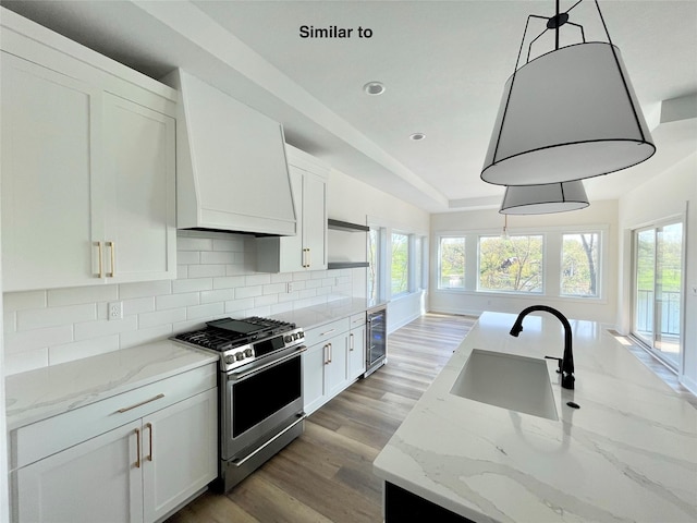 kitchen featuring hanging light fixtures, stainless steel gas range oven, premium range hood, and white cabinets