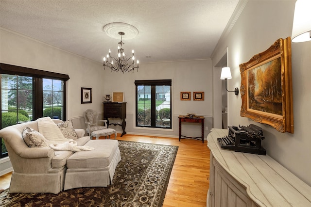 living room featuring an inviting chandelier, ornamental molding, light hardwood / wood-style flooring, and a textured ceiling