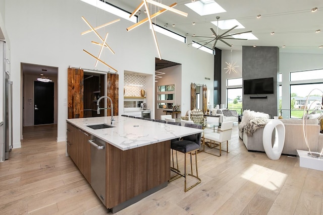 kitchen featuring sink, light hardwood / wood-style flooring, a towering ceiling, a skylight, and a large island with sink