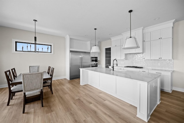 kitchen featuring hanging light fixtures, stainless steel built in refrigerator, gas stovetop, white cabinets, and a center island with sink