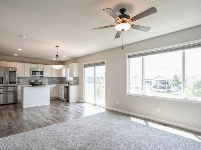 kitchen featuring a kitchen island, appliances with stainless steel finishes, decorative light fixtures, tasteful backsplash, and white cabinets