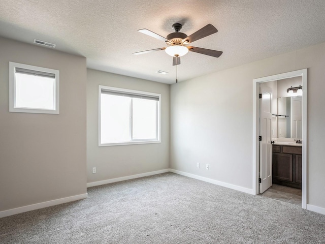 unfurnished bedroom with ceiling fan, ensuite bath, light carpet, and a textured ceiling