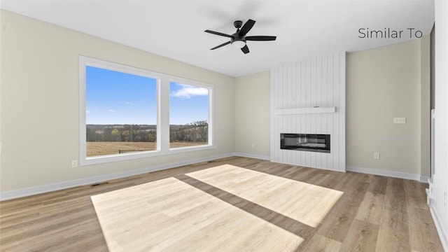 unfurnished living room with a large fireplace, baseboards, light wood finished floors, and a ceiling fan