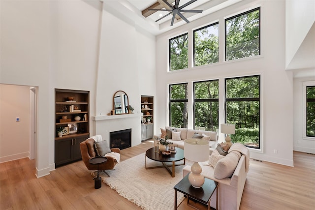 10430 Thorne Dr, West Des Moines, IA 50266 - living room featuring a towering ceiling, a glass covered fireplace, light wood-type flooring, a ceiling fan, and built in shelves