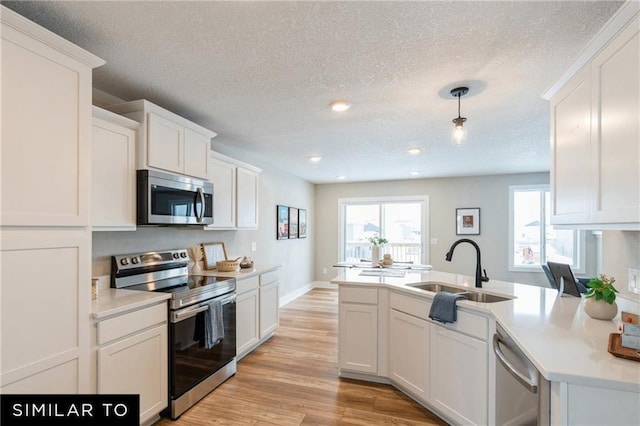 kitchen with sink, white cabinetry, light wood-type flooring, appliances with stainless steel finishes, and pendant lighting