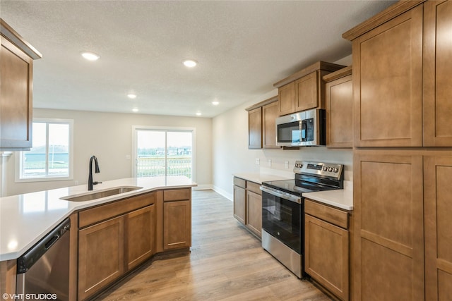 kitchen with light wood-type flooring, light countertops, brown cabinets, a sink, and stainless steel appliances