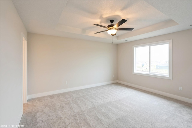 empty room featuring baseboards, a ceiling fan, a tray ceiling, and light carpet