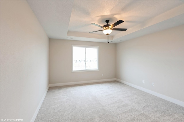 empty room featuring light colored carpet, a ceiling fan, baseboards, and a tray ceiling