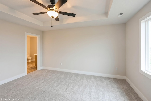 carpeted empty room featuring plenty of natural light, a tray ceiling, ceiling fan, and visible vents