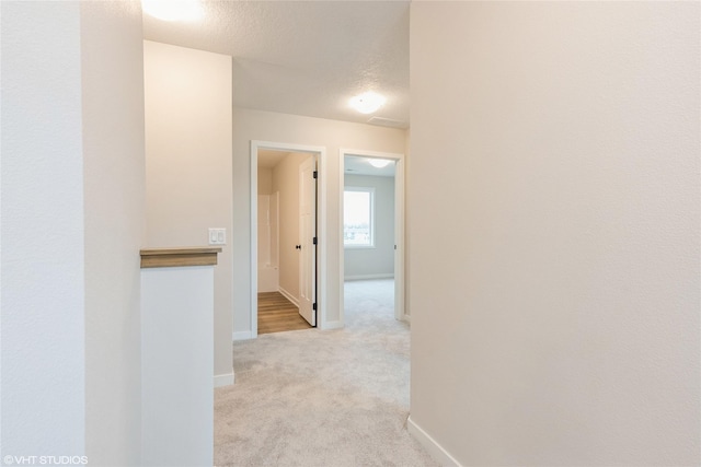 hallway featuring a textured ceiling, baseboards, and light carpet