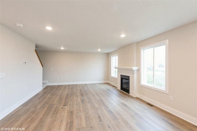 unfurnished living room featuring a glass covered fireplace, baseboards, light wood-type flooring, and recessed lighting