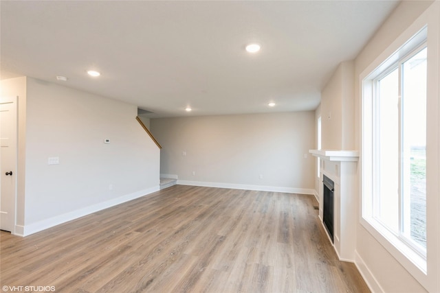 unfurnished living room with a fireplace, recessed lighting, light wood-style flooring, and a wealth of natural light