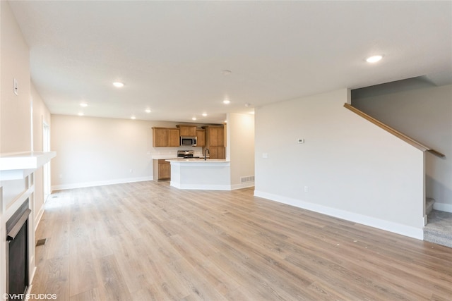 unfurnished living room with visible vents, a sink, baseboards, light wood finished floors, and recessed lighting