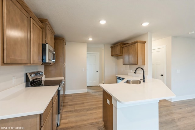 kitchen featuring brown cabinetry, a sink, light wood finished floors, a peninsula, and stainless steel appliances