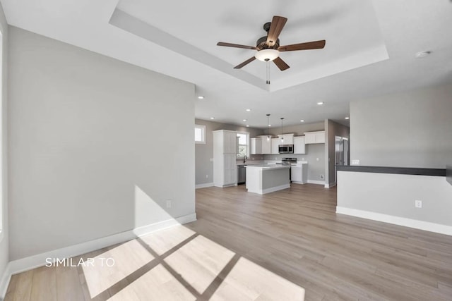 unfurnished living room with ceiling fan, light wood-type flooring, and a tray ceiling