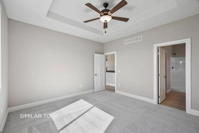 unfurnished bedroom with light colored carpet, a raised ceiling, and ensuite bath