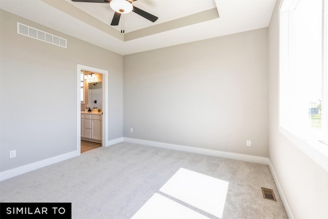 empty room featuring light carpet, ceiling fan, and a tray ceiling