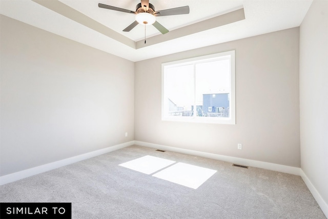 unfurnished room featuring a raised ceiling, ceiling fan, and carpet flooring