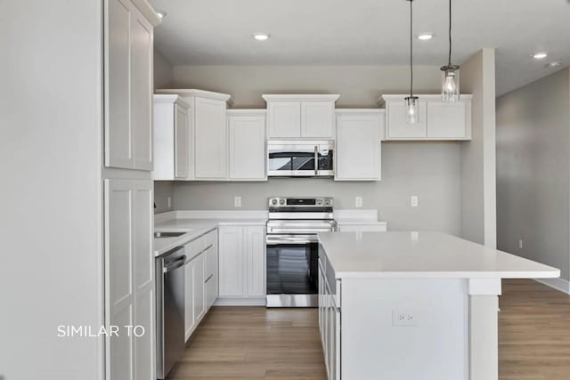 kitchen featuring hanging light fixtures, stainless steel appliances, white cabinets, a kitchen island, and light wood-type flooring