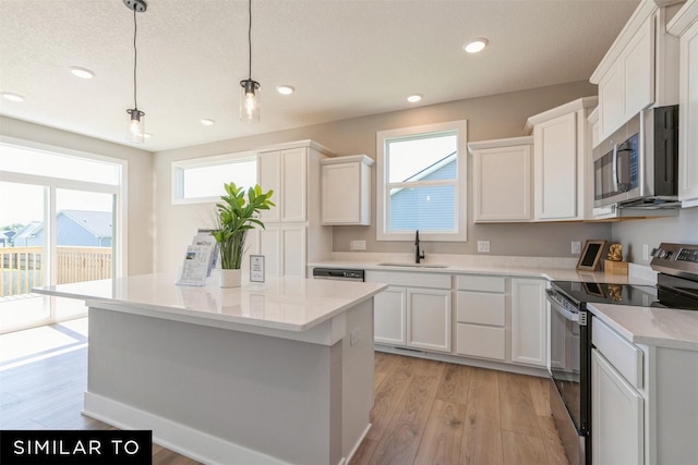 kitchen featuring stainless steel appliances, hanging light fixtures, sink, and white cabinets